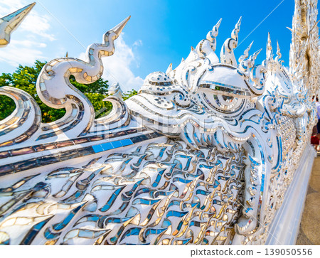 The white temple (Wat Rong Khun) in Chiang Rai city, Thailand. Beautiful buddhist ancient building with bridge above damned souls of sinners, path to the heaven. Famous tourist destination. Blue sky 139050556
