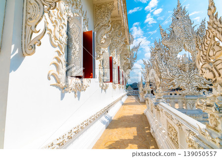 The white temple (Wat Rong Khun) in Chiang Rai city, Thailand. Beautiful buddhist ancient building with bridge above damned souls of sinners, path to the heaven. Famous tourist destination. Blue sky 139050557