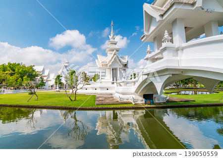 The white temple (Wat Rong Khun) in Chiang Rai city, Thailand. Beautiful buddhist ancient building with bridge above damned souls of sinners, path to the heaven. Famous tourist destination. Blue sky 139050559