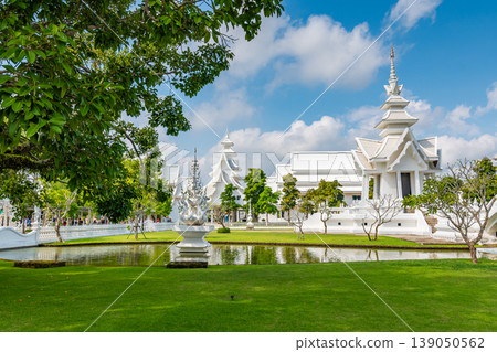 The white temple (Wat Rong Khun) in Chiang Rai city, Thailand. Beautiful buddhist ancient building with bridge above damned souls of sinners, path to the heaven. Famous tourist destination. Blue sky The white temple (Wat Rong Khun) in Chiang Rai city, Thailand. Beautiful buddhist ancient building with bridge above damned souls of sinners, path to the heaven. Famous tourist destination. Blue sky 139050562