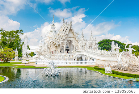 The white temple (Wat Rong Khun) in Chiang Rai city, Thailand. Beautiful buddhist ancient building with bridge above damned souls of sinners, path to the heaven. Famous tourist destination. Blue sky 139050563