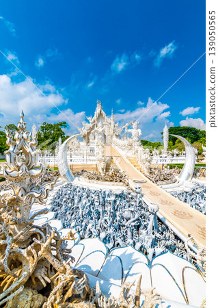 The white temple (Wat Rong Khun) in Chiang Rai city, Thailand. Beautiful buddhist ancient building with bridge above damned souls of sinners, path to the heaven. Famous tourist destination. Blue sky 139050565