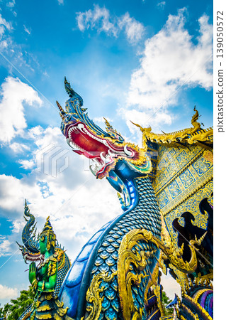 Statue of dragon at Wat Rong Suea Ten temple (blue temple) near Chiang Rai city, Thailand. Mystical sculpture of ancient beast. View from bottom with blue sky dynamic background Statue of dragon at Wat Rong Suea Ten temple (blue temple) near Chiang Rai city, Thailand. Mystical sculpture of ancient beast. View from bottom with blue sky dynamic background 139050572