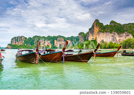 The famous Railay beach at Krabi, Thailand. Long tailed boats are prepared for passengers near limestone rock. Tropical paradise, famous tourist destination. Turquoise sea with white sand The famous Railay beach at Krabi, Thailand. Long tailed boats are prepared for passengers near limestone rock. Tropical paradise, famous tourist destination. Turquoise sea with white sand 139050601