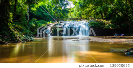 Beautiful waterfall Mae Sa, Thailand. Fresh and pure water stream is flowing on the rock stone ground in tropical rainforest. Fresh plants and trees above river. Vibrant colors in pure nature Beautiful waterfall Mae Sa, Thailand. Fresh and pure water stream is flowing on the rock stone ground in tropical rainforest. Fresh plants and trees above river. Vibrant colors in pure nature 139050655