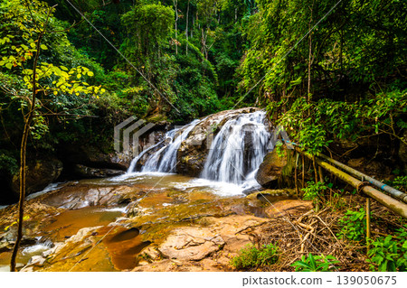 Beautiful waterfall Mae Sa, Thailand. Fresh and pure water stream is flowing on the rock stone ground in tropical rainforest. Fresh plants and trees above river. Vibrant colors in pure nature Beautiful waterfall Mae Sa, Thailand. Fresh and pure water stream is flowing on the rock stone ground in tropical rainforest. Fresh plants and trees above river. Vibrant colors in pure nature 139050675