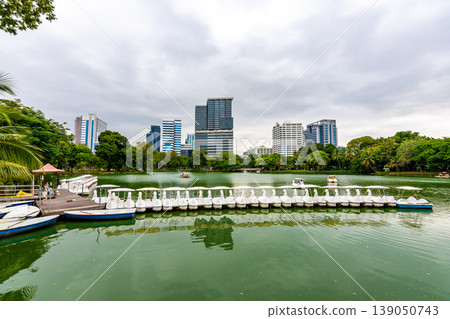 Bangkok cityscape view from Lumpini park in city center. Panoramic photo of skyscrapers and futuristic buildings from metal and glass. View from the small lake in Lumpini park. Fresh green plants. Bangkok cityscape view from Lumpini park in city center. Panoramic photo of skyscrapers and futuristic buildings from metal and glass. View from the small lake in Lumpini park. Fresh green plants. 139050743