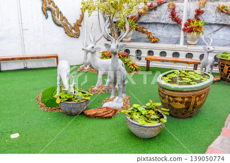 Small deer statues with white color placed on green ground. Waterlily in the pot. Small deer statues with white color placed on green ground. Waterlily in the pot. 139050774