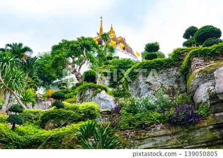 Small garden with water pond, Buddha statue and flowers near the Wat Saket temple (Golden mount) in Bangkok, Thailand. Famous religion building on top of the mountain in center of city. Small garden with water pond, Buddha statue and flowers near the Wat Saket temple (Golden mount) in Bangkok, Thailand. Famous religion building on top of the mountain in center of city. 139050805