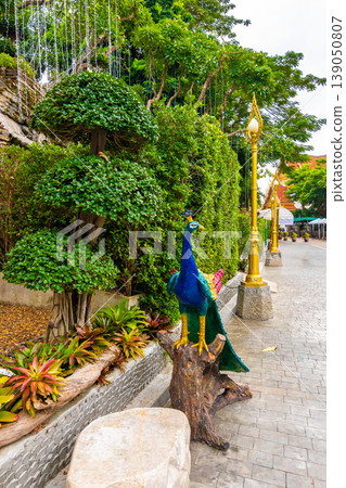Statue of peacock near Wat Saket temple in Bangkok city. Statue is placed near the buddhist garden with fresh green trees and flowers. Beautiful spirituality, vibrant colors, Thai culture Statue of peacock near Wat Saket temple in Bangkok city. Statue is placed near the buddhist garden with fresh green trees and flowers. Beautiful spirituality, vibrant colors, Thai culture 139050807