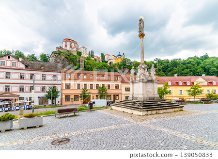 Plague column statue in Vranov village, czech republic. View from main square to Vranov castle placed on big rock. Cloudy weather. Plague column statue in Vranov village, czech republic. View from main square to Vranov castle placed on big rock. Cloudy weather. 139050833