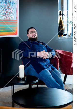 Chef reclining in lounge, relaxed after service with candle and champagne nearby, soft evening lighting and contemporary interior create Chef reclining in lounge, relaxed after service with candle and champagne nearby, soft evening lighting and contemporary interior create 139051260
