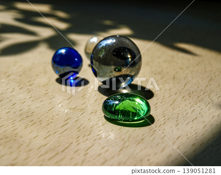 Multicolored glass balls in bright sun rays. Macro shot featuring optical refraction, spectral light and vibrant chromatic spheres. Rhythmic composition with brilliant glares and reflections Multicolored glass balls in bright sun rays. Macro shot featuring optical refraction, spectral light and vibrant chromatic spheres. Rhythmic composition with brilliant glares and reflections 139051281