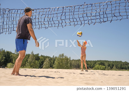 A child gives a ball to his father in a game of beach volleyball. Dad trains his daughter. Active sports and family holidays during the summer holidays. 139051291