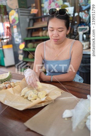 Woman Enjoying Durian at a Vibrant Market Buffet with Refreshing Drink Woman Enjoying Durian at a Vibrant Market Buffet with Refreshing Drink 139051799