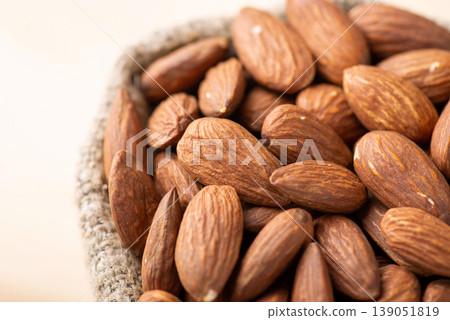 Top view of almonds in small bag. Close up shot of fresh tasty almond nuts in bag made of linen fiber on light background Top view of almonds in small bag. Close up shot of fresh tasty almond nuts in bag made of linen fiber on light background 139051819