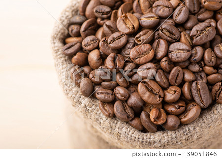 Close up of coffee beans in linen sack. Roasted aromatic coffee grain in bag made of linen fiber Close up of coffee beans in linen sack. Roasted aromatic coffee grain in bag made of linen fiber 139051846