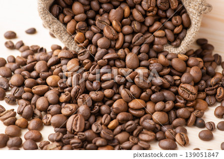 Roasted coffee beans fell from small bag on wooden table. Fresh roasted aromatic coffee beans Roasted coffee beans fell from small bag on wooden table. Fresh roasted aromatic coffee beans 139051847