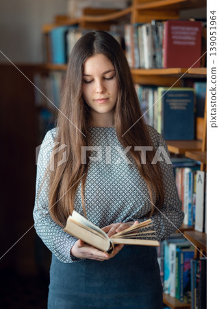 Portrait of a student girl reading a book in library. Young girl looking through a book in university library 139051964