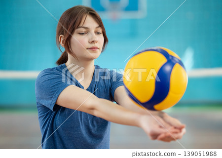 Young girl playing volleyball indoors. Shot of a female practicing volleyball skills, training digging with a ball Young girl playing volleyball indoors. Shot of a female practicing volleyball skills, training digging with a ball 139051988