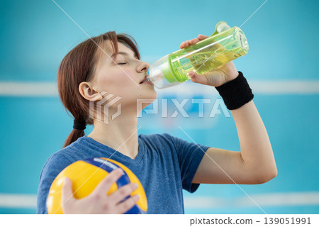 Young girl drinking water while having volleyball training on the court. Stay hydrated doing sport and physical activities Young girl drinking water while having volleyball training on the court. Stay hydrated doing sport and physical activities 139051991