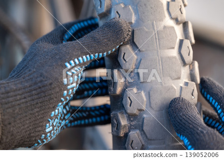 Male hands in gloves examine the worn Enduro motorcycle tires. Two-wheeled vehicle, which has been in a lot of use, tires need to be replaced 139052006