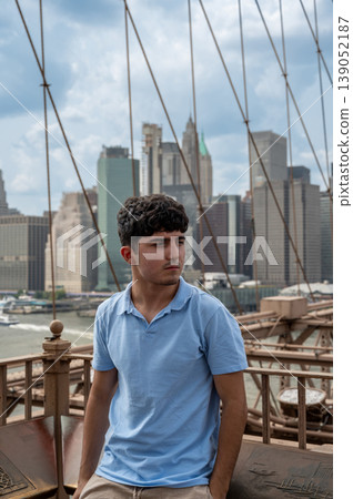 New york, usa august 15,2024. Young man standing on brooklyn bridge, gazing across east river at manhattan skyline on a clear summer day, urban sightseeing New york, usa august 15,2024. Young man standing on brooklyn bridge, gazing across east river at manhattan skyline on a clear summer day, urban sightseeing 139052187