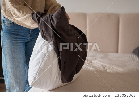 Person putting duvet into dark cover while making bed in bedroom. Concept of home routine 139052365