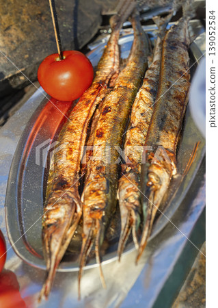 Grilled garfish from Black Sea served whole on metal tray, charred skin prepared in outdoor street food setting in Bulgaria. Seafood cooking, grilled garfish, Black Sea cuisine, street food culture 139052584