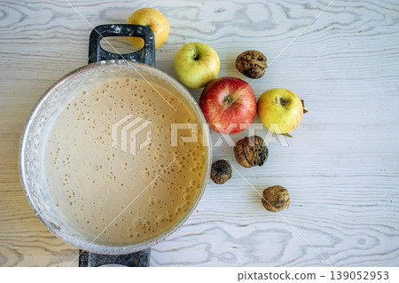 Top view of the vintage pot with homemade apple pie batter on a rustic white wooden table, surrounded by fresh apples and walnuts. Top view of the vintage pot with homemade apple pie batter on a rustic white wooden table, surrounded by fresh apples and walnuts. 139052953