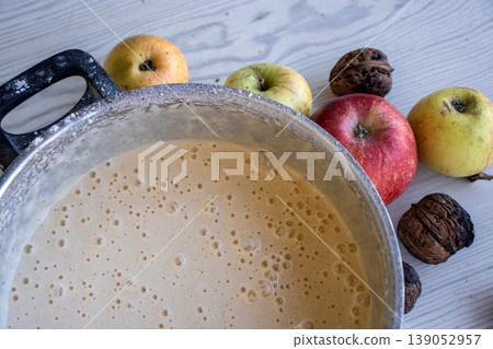 Top view of the vintage pot with homemade apple pie batter on a rustic white wooden table, surrounded by fresh apples and walnuts. Top view of the vintage pot with homemade apple pie batter on a rustic white wooden table, surrounded by fresh apples and walnuts. 139052957