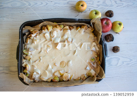 Apple pie batter poured over sliced apples in a baking pan, with rustic background, alongside fresh apples and walnuts. Apple pie batter poured over sliced apples in a baking pan, with rustic background, alongside fresh apples and walnuts. 139052959