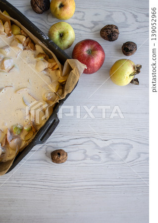 Apple pie batter poured over sliced apples in a baking pan, with rustic background, alongside fresh apples and walnuts. Apple pie batter poured over sliced apples in a baking pan, with rustic background, alongside fresh apples and walnuts. 139052966