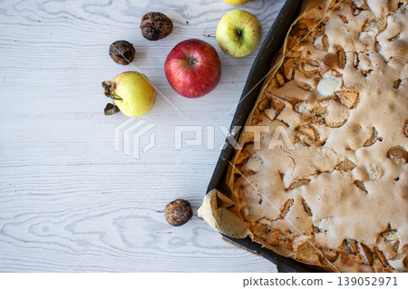 Homemade apple cake with a golden crust in a baking tray, placed on a rustic white wooden table with fresh apples and walnuts Homemade apple cake with a golden crust in a baking tray, placed on a rustic white wooden table with fresh apples and walnuts 139052971