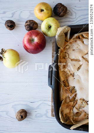 Homemade apple cake with a golden crust in a baking tray, placed on a rustic white wooden table with fresh apples and walnuts Homemade apple cake with a golden crust in a baking tray, placed on a rustic white wooden table with fresh apples and walnuts 139052974