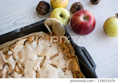 Homemade apple cake with a golden crust in a baking tray, placed on a rustic white wooden table with fresh apples and walnuts Homemade apple cake with a golden crust in a baking tray, placed on a rustic white wooden table with fresh apples and walnuts 139052976