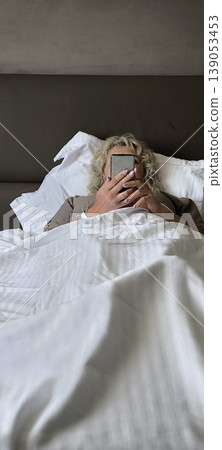 Calm morning: woman checking phone in bed Calm morning: woman checking phone in bed 139053453