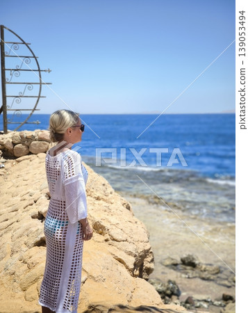 A woman in a beach tunic looks out over the sea from a cliff A woman in a beach tunic looks out over the sea from a cliff 139053494