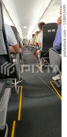 Passengers in the cabin of an airplane before takeoff or after landing, view from the aisle 139053495