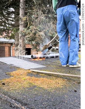 Roof repair and installation of roll roofing using a gas torch on the roof of a building. Roof repair and installation of roll roofing using a gas torch on the roof of a building. 139053524