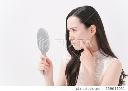 A woman looking in the mirror and troubled by skin problems. 139055031