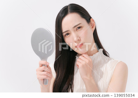 A woman looking in the mirror and troubled by skin problems. A woman looking in the mirror and troubled by skin problems. 139055034