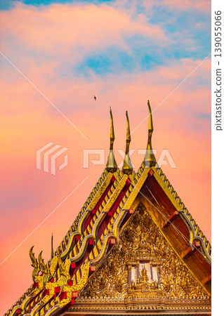 Golden temple roof details against a vibrant sunset sky with a bird flying Golden temple roof details against a vibrant sunset sky with a bird flying 139055066