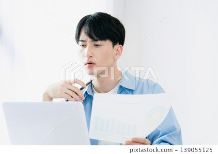 一位年輕人一邊看著文件一邊思考。 139055125
