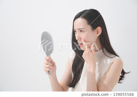 一位女士對著鏡子,為皮膚問題而煩惱。 一位女士對著鏡子,為皮膚問題而煩惱。 139055588