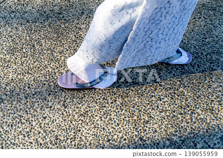 view of person wearing traditional Japanese tabi socks and purple zori sandals walking on a pebble stone path. Part of a light blue lace kimono is visible. Cultural fashion shot. 139055959