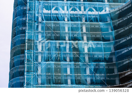 Exterior view of a high-rise building under construction, covered with protective sheeting. Exterior view of a high-rise building under construction, covered with protective sheeting. 139056328