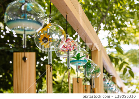 Glass wind chimes lined up in a wooden frame and the greenery of summer Glass wind chimes lined up in a wooden frame and the greenery of summer 139056330