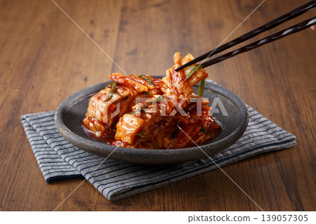 The image shows someone lifting up kimchi with chopsticks. The image shows someone lifting up kimchi with chopsticks. 139057305