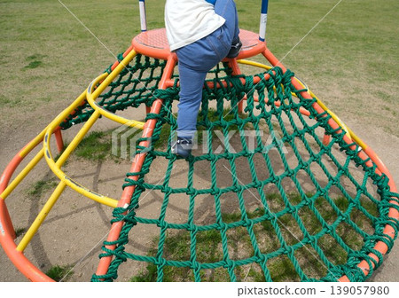 The back view of a child climbing to the top of an athletic playground structure. 139057980
